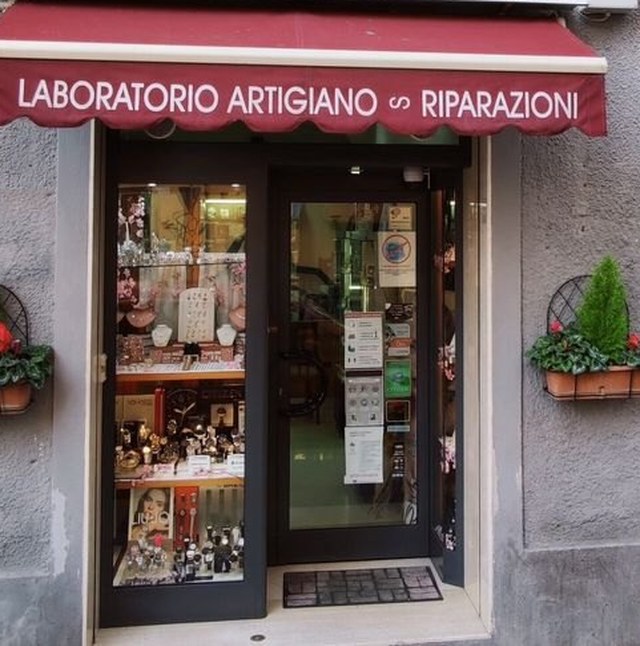 L’ingresso del negozio: la tenda rossa con la scritta Laboratorio artigiano, riparazioni, e la vetrina